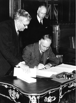 The Australian Prime Minister, John Curtin, signs the Australia–New Zealand Agreement, Canberra, 21 January 1944, watched by the Australian Minister for External Affairs and Attorney-General, Dr Herbert V Evatt (left), and the New Zealand Prime Minister, Peter Fraser. [National Library of Australia]