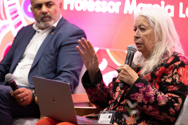 Panel discussion at a NAIDOC Week speaker event, with a speaker holding a microphone while another panel member listens beside them.