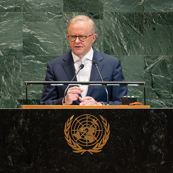 Photograph shows Australian Prime Minister Anthony Albanese speaking at a United Nations podium. Green marble backdrop, dual microphones, papers, and gold UN emblem on black lectern identify formal diplomatic address.