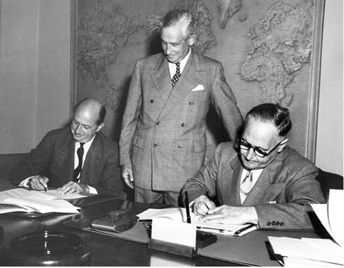 The Australian Ambassador to the United States, Norman JO Makin (right), and the President of the International Bank for Reconstruction and Development, Eugene R Black (left), sign the documents for a $100 million loan to Australia, watched by the Vice President of the International Bank, Robert L Garner, Washington DC, 22 August 1950. [World Bank]