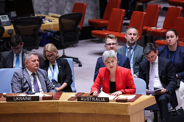 Photograph shows an international meeting room, with Australian and Ukrainian delegates seated at labeled tables. Australian representative in a red blazer speaks at a desk, surrounded by officials, laptops, microphones, and rows of red chairs.