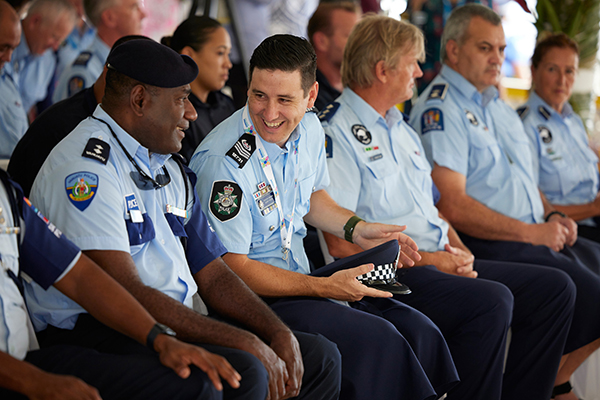 Photograph shows uniformed police officers seated in a row during a formal event, with two foreground officers smiling and conversing.