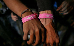 Two hands shown with pink armbands. The text on the armband includes the text Australian Government Aid Program and MTV Exit.