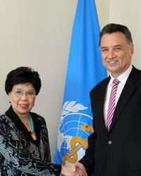 Dr Emerson and World Health Organization Chief, Margaret Chan shaking hands in front of a World Health Organization flag.