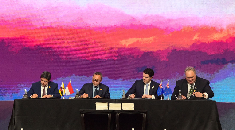 Group photo of officials signing documents onstage. 