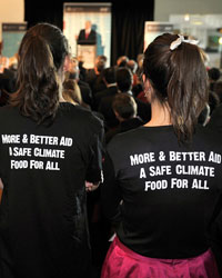 Photo of two women dressed in black T-Shirts with label 'More & Better Aid A Safe Climate Food for All' on the shirt