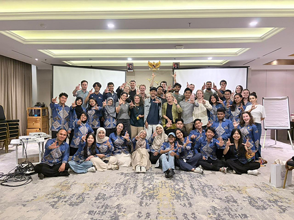 Group photo of exchange program delegates inside a conference room, with participants standing and seated in front of a presentation screen during an orientation session.