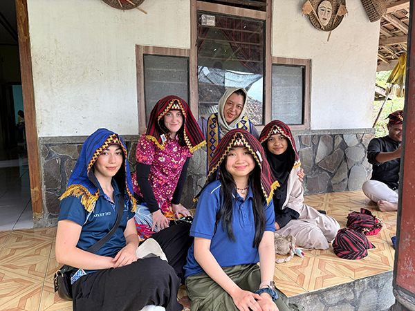 Program delegates seated on a veranda wearing traditional Lampung attire, posed together outside a house with local decorative elements visible.