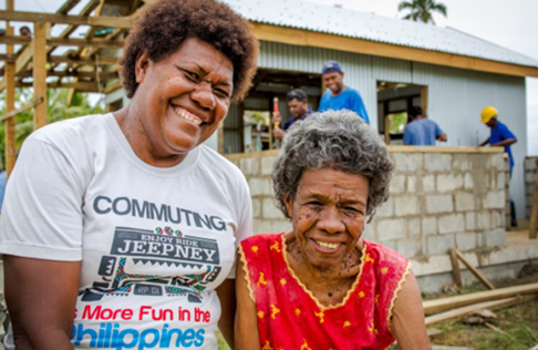 Two women standing in front of people building a house