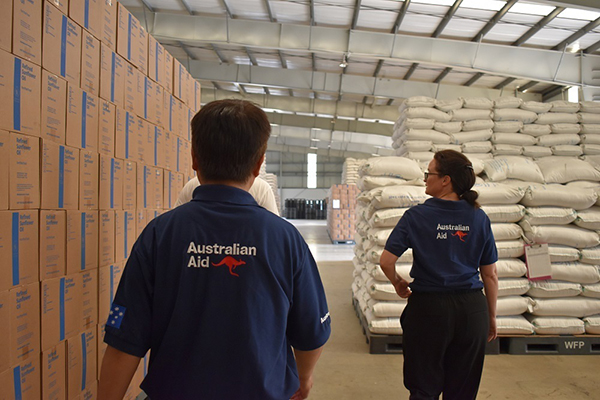 Two people walking through a warehouse wearing Australian Aid shirts. 