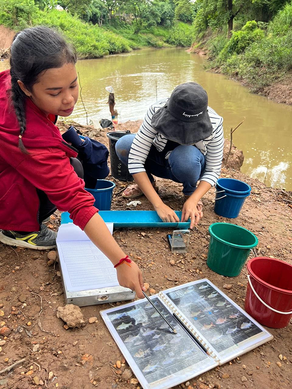 Two people at a river studying fish.