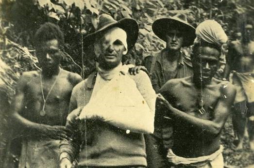 Black and white image of injured Australian soldier being supported PNG locals.