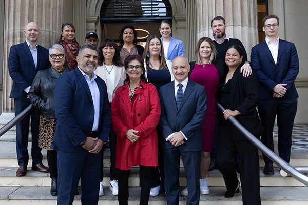 Group of people in formal and semi-formal attire standing on steps outside a grand building with columns.