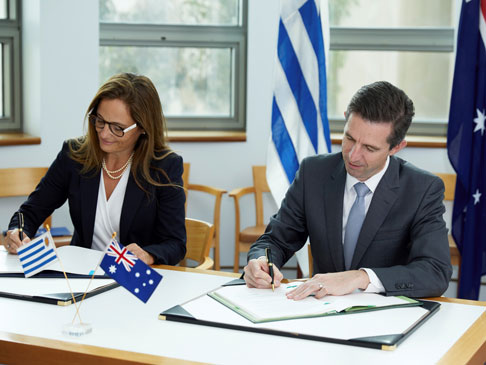 Two people sitting at a desk, signing paper work.