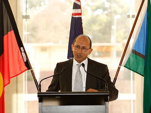 Peter Varghese speaking at a podium in front of the Aboriginal, Australian and Torres Strait Islander flags.