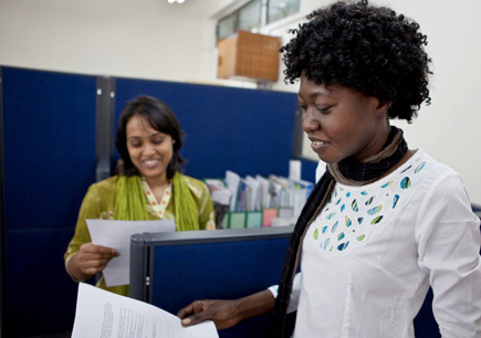 Two smiling women in office look through printed papers