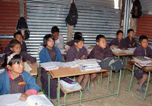 Students sitting in temporary classroom with iron sheets as walls.
