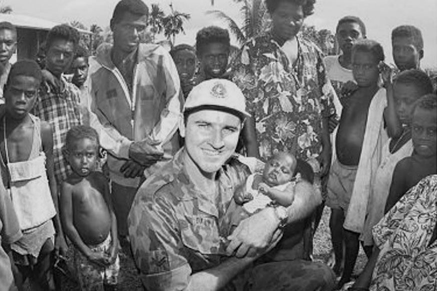 Australian military officer holding baby while in a crowd of people