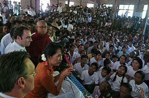 Aung San Suu Kyi with others on a podium, speaking to a crowd.