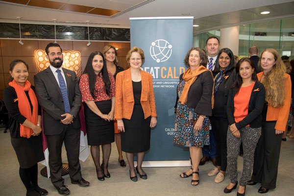 Group of staff wearing orange and standing with a DFAT CALD Network banner