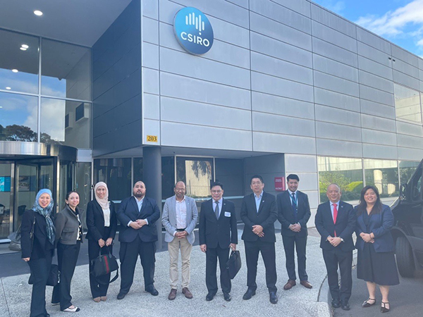 A group of ten people in formal attire standing in front of a modern building with the blue and white CSIRO logo in front of the building entrance.