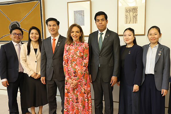 Seven people in business attire stand smiling side-to-side for a photograph. They are inside a meeting room with First Nations artwork hanging on the wall in the background.