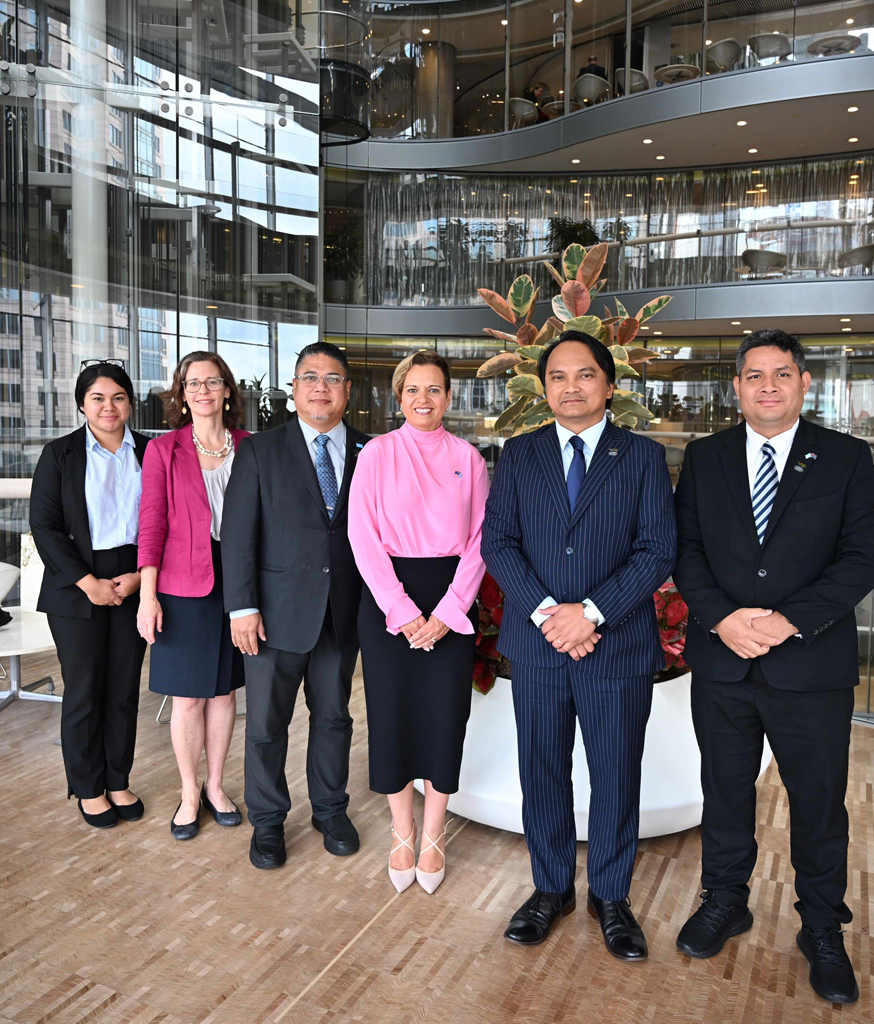 A group of five people stand side by side with one Australian minister, posing for a photo in a large foyer. 