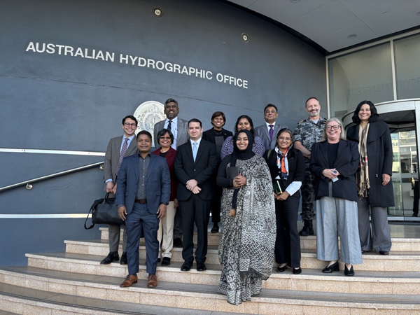 A group of 13 people stand on steps at the entrance of an office building, posing for a photo.