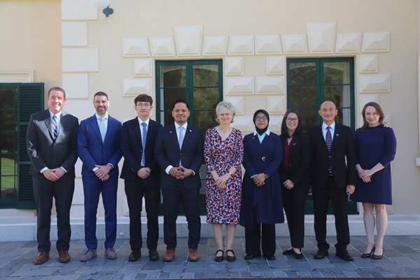 Nine people in business attire stand outside side-by-side for a photograph in front of the Government House building in Adelaide.