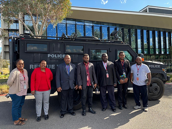 Seven people in business attire stand outside in front of a police rescue vehicle, with an office building in the background.