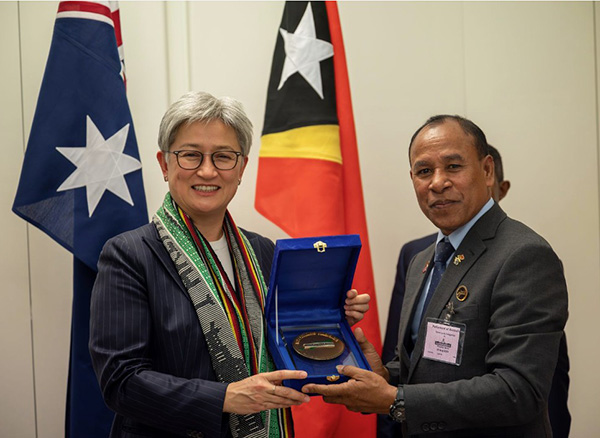 The head of delegation presenting the Australian Foreign Minister with a small gift. Both are smiling and standing in front of the Australian and Timor-Leste flags