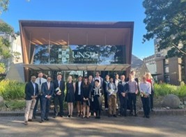 Eighteen people, comprising the Indian delegation and university staff, standing in front of a building bearing a University of Sydney logo.