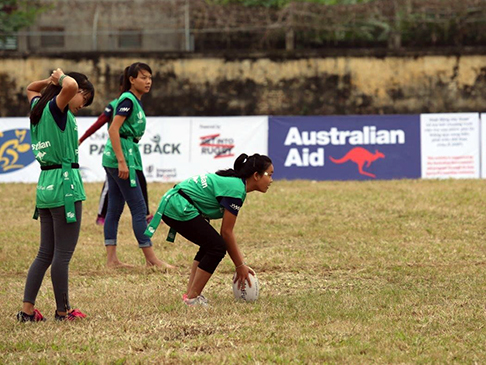 Young women on a football field, with an Australian Aid banner in the background