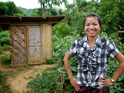 Lady smiling in Laos outback in front of outdoor toilet facility
