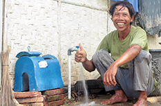 Man smiling with thumbs up in front of water tap