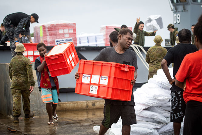 Residents of Tanna Island, alongside ship’s company from HMAS Canberra, unload Australian Aid humanitarian assistance. The red boxes being unloaded are Kitchen Kits. Kitchen Kits provide essential supplies – such as buckets and cooking pots and utensils – to support a household to cook basic meals and store drinking water. 