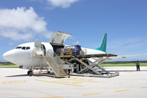 Large aeroplane on tarmac with palettes of large well-wrapped packages being unloaded.