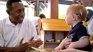 Man from PNG wearing hearing aid communicates with young child wearing hearing aid