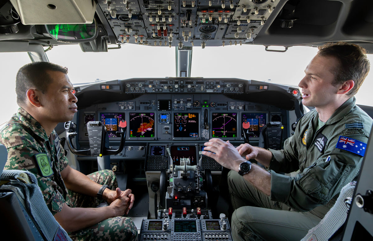 Photograph shows two uniformed pilots inside a modern aircraft cockpit during an apparent briefing or training session.