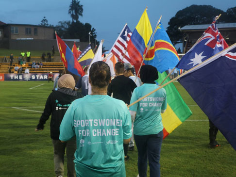 Photo of people walking onto a field, each holding different country flags.