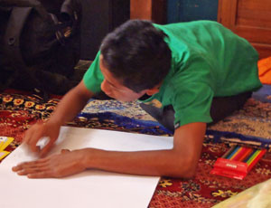 Young boy on floor drawing on large sheet of white paper