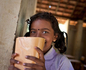 A girl smiles behind her schoolbook at a school in Sri Lanka.