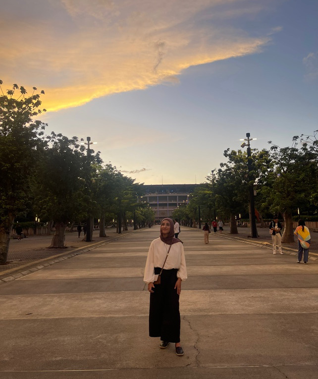 Fatima standing in between a row of trees