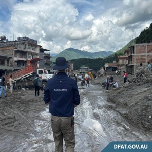 An Australian official stands in front of a flood-devastated village.