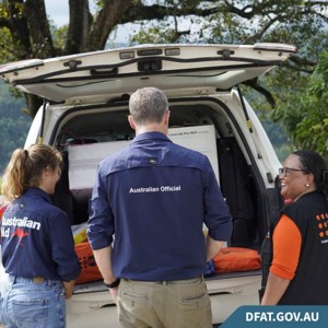 3 officials standing at the back of a car with humanitarian supplies.