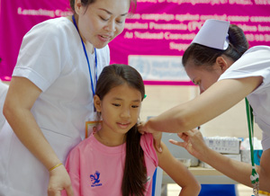 Smiling girl just about to the vaccinated by a nurse, with a second nurse assisting
