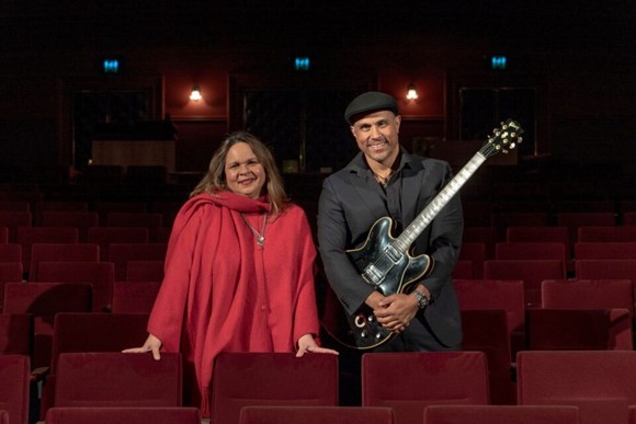 Singer on the left and guitarist on the right, standing amongst audience seats