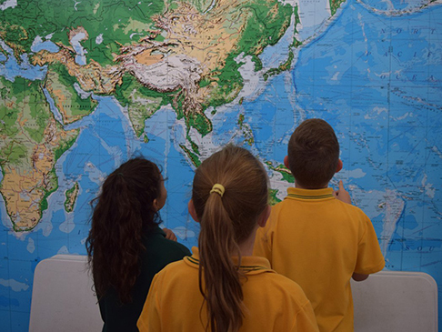 3 school-aged children looking at a large map of the world