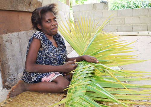 Photo of Helen, a person with disability weaving a plant.