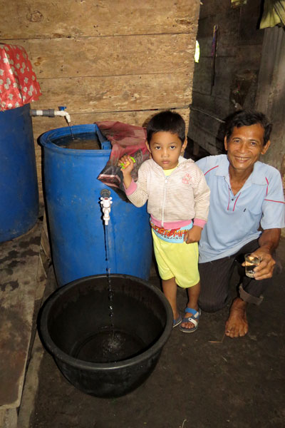 Father and child filling a bucket with water from a tank.